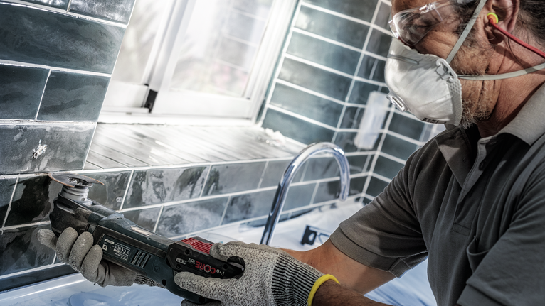 一名配戴安全設備的人員使用電動工具切割水槽附近的磁磚。