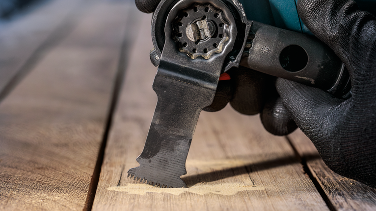 配戴安全設備的人使用多功能工具切割木材。