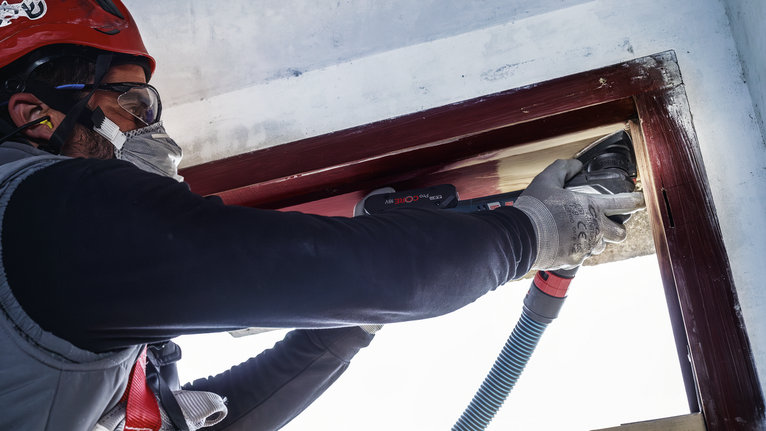 一名配戴安全設備的人員正在使用電動工具打磨木製窗框。