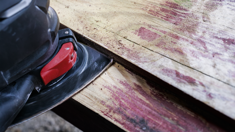 電動砂光機正在打磨一塊風化的木板。