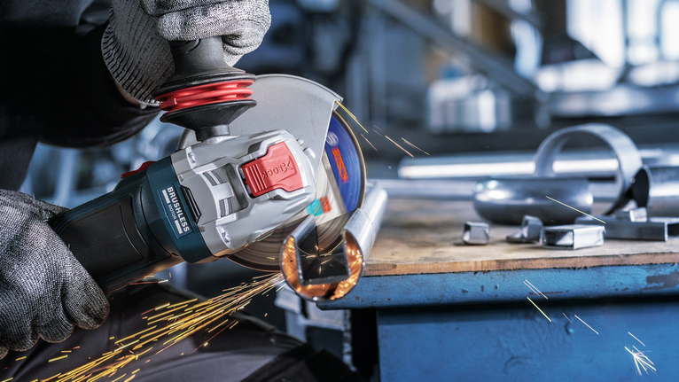 一名配戴安全設備的人正在研磨金屬管，產生火花。