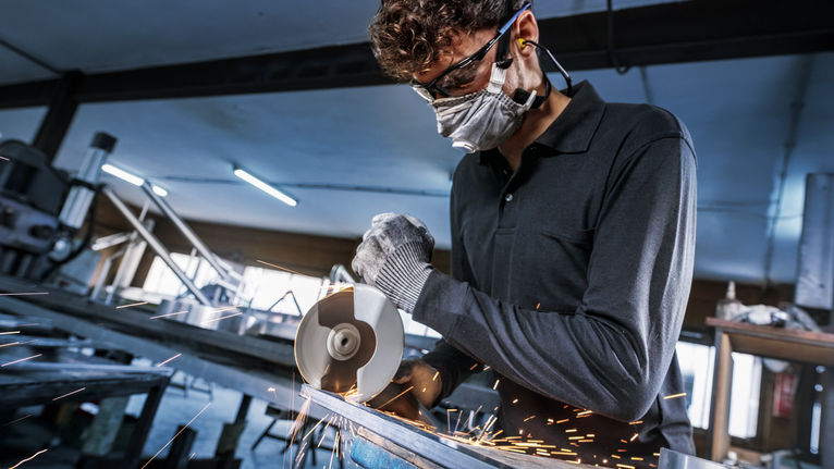 配戴安全設備的人用角磨機切割金屬，火花四濺。