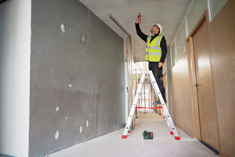 A person wearing safety equipment marks the ceiling using a laser leveling tool.