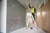 A person wearing safety equipment marks the ceiling using a laser leveling tool.