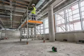 A person wearing safety equipment stands on scaffolding while using a laser leveling tool.