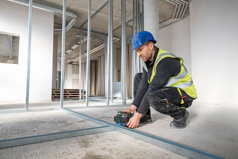 A person wearing safety equipment aligns metal studs using a laser leveling tool.
