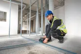A person wearing safety equipment aligns metal studs using a laser leveling tool.