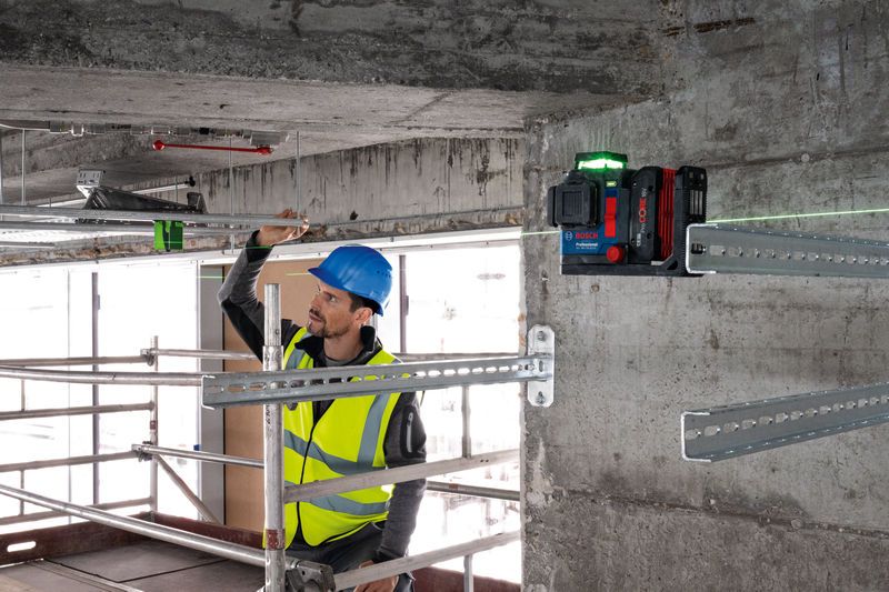A person wearing safety equipment aligns metal framing using a laser leveling tool.