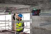 A person wearing safety equipment aligns metal framing using a laser leveling tool.