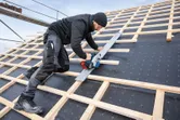 一名佩戴安全設備的人員使用無線圓鋸在陡峭的屋頂上切割木材。.