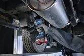 一名配戴安全設備的人員使用無線衝擊扳手對車輛底盤進行操作。