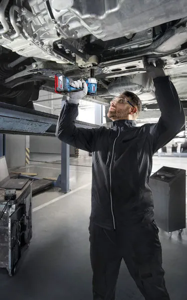 一名配戴安全設備的人員使用電鑽在升起的車輛下方作業。.
