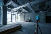 在建築工地上，一名配戴安全設備的人員正在使用雷射調平工具調整牆壁。
