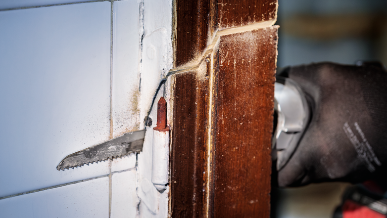 配戴安全設備的人員用往復鋸切割木門框。