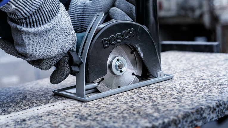 一名佩戴安全設備的人員使用金屬鋸切割花崗岩板。