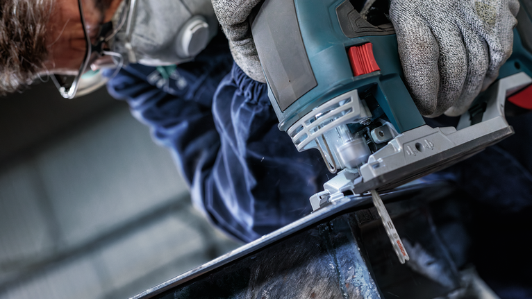 配戴安全設備的人使用曲線鋸切割金屬。