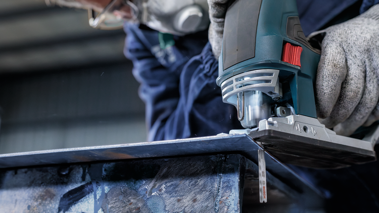 配戴安全設備的人使用曲線鋸切割金屬板。