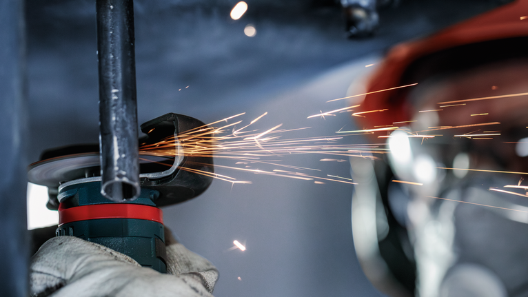 PRO Stainless Steel and Metal 接合切削砂輪片,76 x 1 x 10 mm 工人配戴安全設備研磨金屬管,產生火花。.