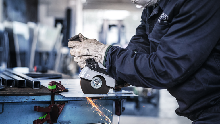 配戴安全設備的人使用角磨機切割金屬，產生火花。