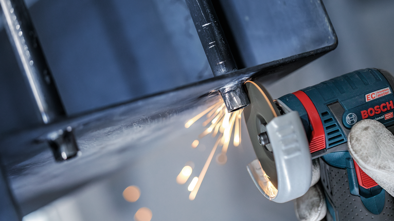 一名佩戴安全設備的人正在研磨金屬梁，產生火花。