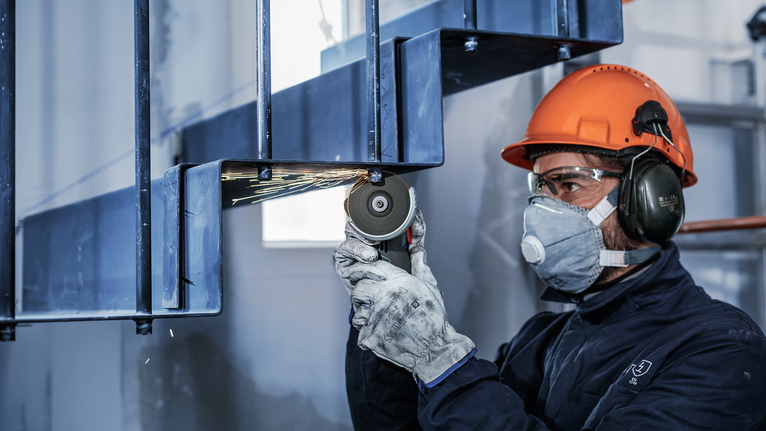 一名佩戴安全設備的人正在研磨金屬梁，產生火花。