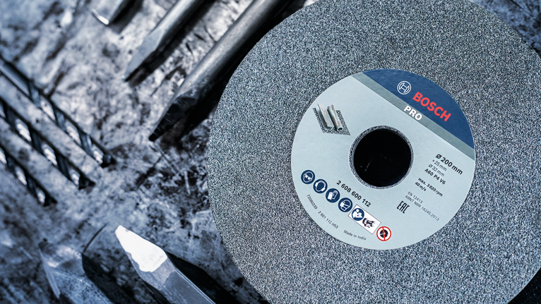 PRO Metal 研磨輪,200 x 25 x 32 mm,G36 大型砂輪放置在粗糙工作表面上的幾個金屬鑽頭之間。