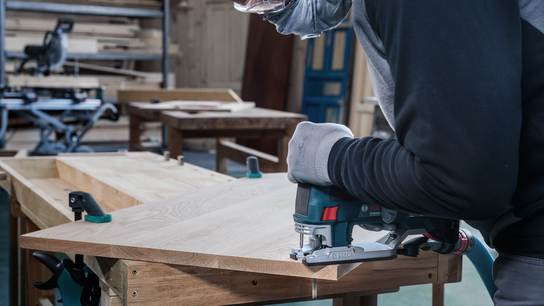 一名佩戴安全設備的工人在車間用曲線鋸切割木材。