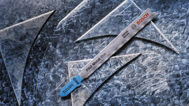 用於切割薄金屬的曲線鋸刀片放在有刮痕的金屬板上。