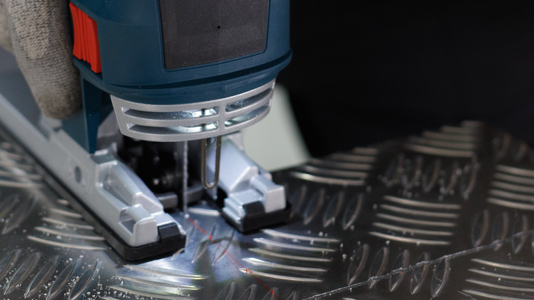 配戴安全設備的人員操作曲線鋸切割有圖案的金屬板。