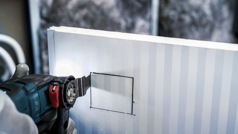 配戴安全設備的人員使用電動工具在幹牆上切割方形開口。