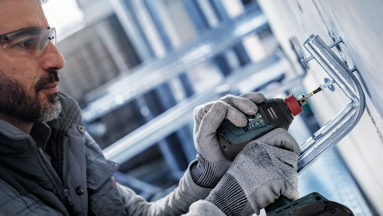 一名配戴安全設備的人使用電鑽將金屬支架固定在牆上。