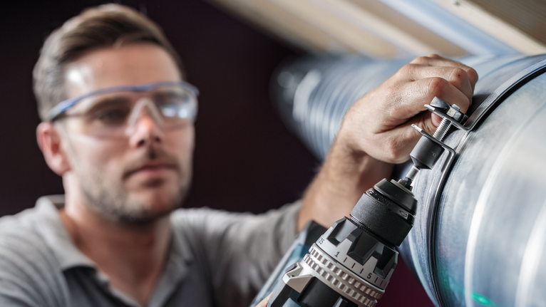 配戴安全設備的人員使用電鑽將螺栓緊固到金屬管道上。