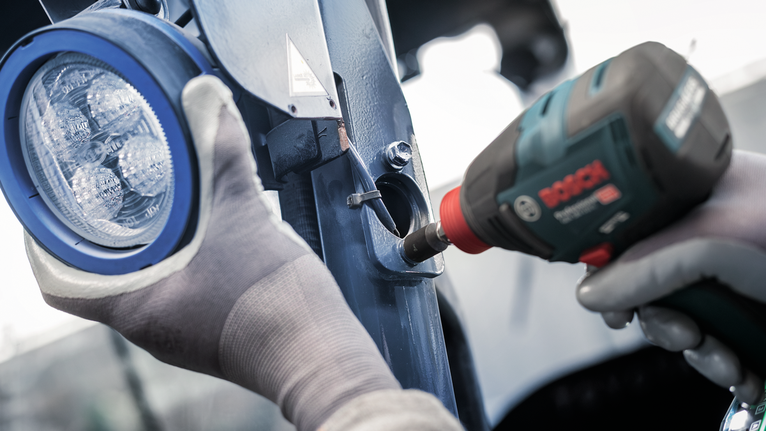 配戴安全設備的人員使用電動工具將金屬支架固定在燈附近。