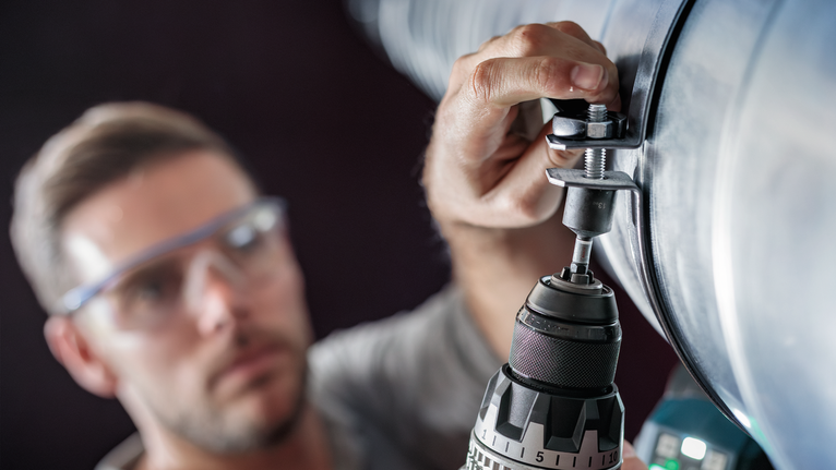 穿著安全設備的人員在一根大金屬管上鑽孔。