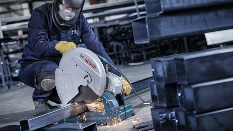 一名配戴安全設備的工人用電鋸切割金屬管道，產生火花。.