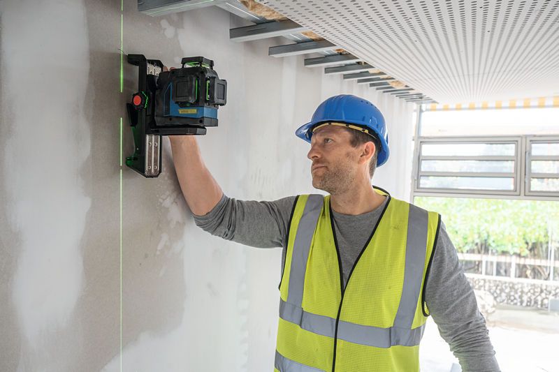 一名佩戴安全設備的人將雷射調平工具對準牆壁。.