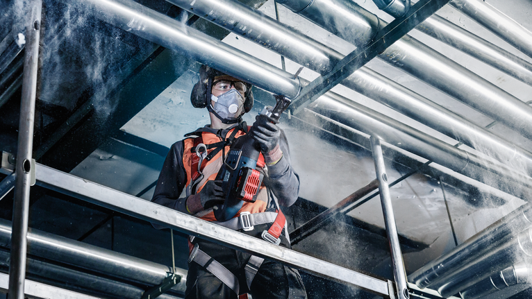 一名配戴安全設備的人員在工業鷹架上鑽入金屬管路。