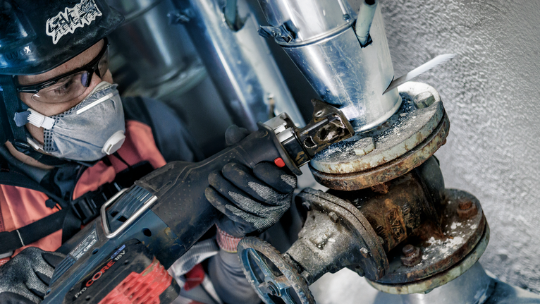 一名配戴安全設備的人員用往復鋸切割金屬管。