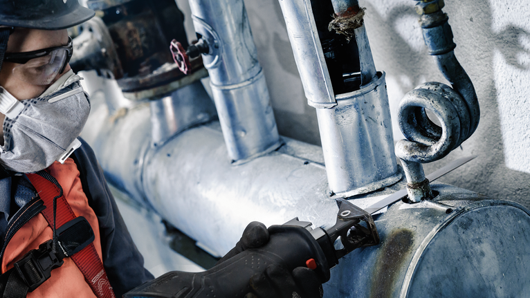 配戴安全設備的人員使用電動工具切割金屬管路。