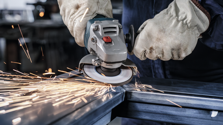 工人穿著安全裝備打磨鋼樑，產生火花。.