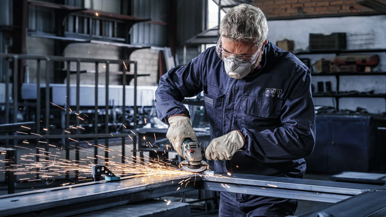 一名戴著安全設備的工人在車間研磨金屬，產生火花。.