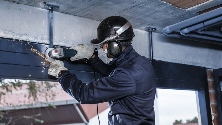 一名佩戴安全設備的人正在磨削鋼樑，產生火花。