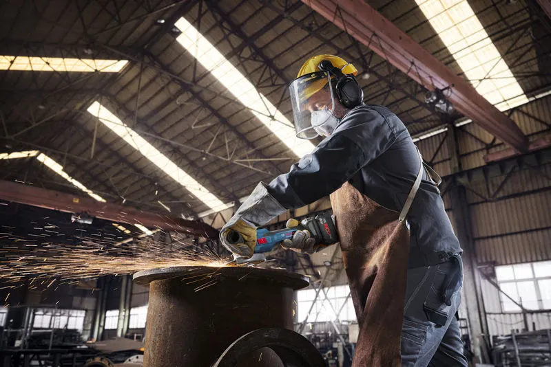一名配戴安全設備的人使用無線角磨機切割金屬，產生火花。.
