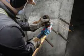 A person wearing safety equipment grinds exposed rebar on a concrete wall.