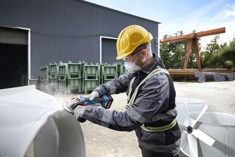 一名佩戴安全裝備的人員在工業現場的戶外打磨金屬。.