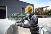 一名佩戴安全裝備的人員在工業現場的戶外打磨金屬。