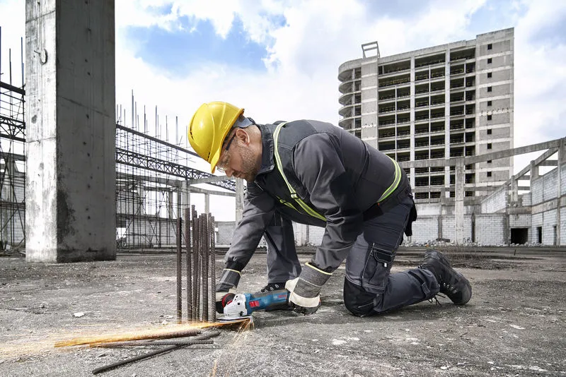 在建築工地上，一名配戴安全設備的工人正在用電動工具切割鋼筋。.