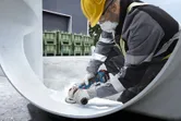 一名配戴安全設備的人正在研磨一根大金屬管的內部。.
