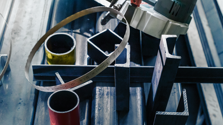 帶鋸放置在工作台上各種金屬管和金屬棒的上方。.