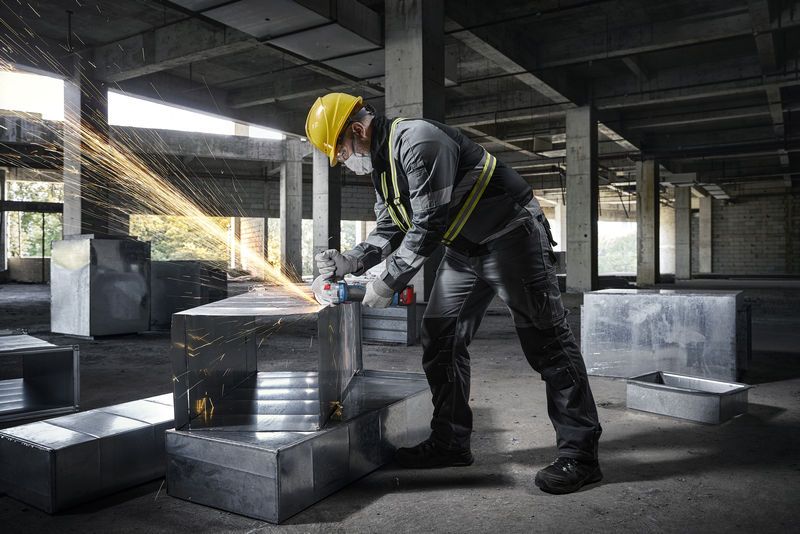 一名配戴安全設備的人員在建築工地上使用角磨機打磨金屬管路。.